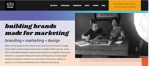 Website banner of BTD Brand showing two professionals discussing over documents, emphasizing their focus on 'building brands made for marketing' with a blend of branding, marketing, and design.