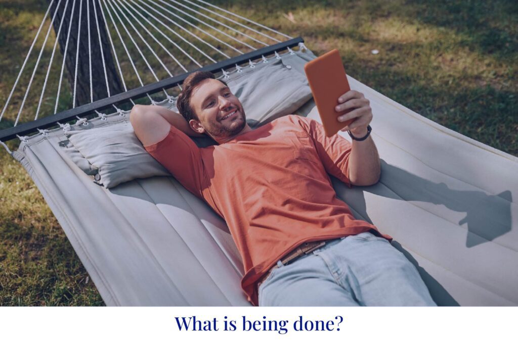 A guy is lying in a hammock with a tablet, under the words 'What is being done?' He looks like he's having a good break from work.