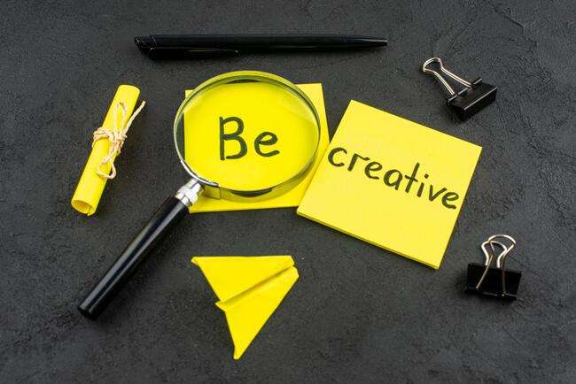 Magnifying glass on 'Be creative' notes symbolizes targeted web design creativity.