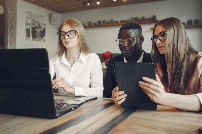 Three professionals working together on a laptop and tablet, focused on immigration case management software.