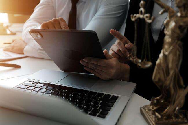 Two professionals discussing over a tablet with a laptop on the desk, symbolizing efficient immigration case management.