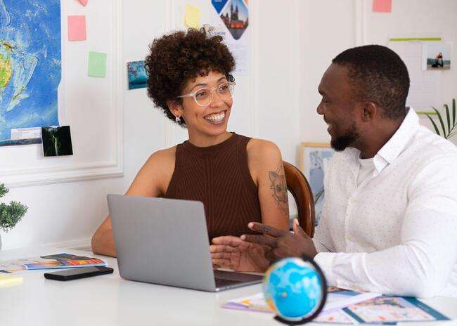  Two people having a discussion in front of a laptop, surrounded by travel documents and a globe, highlighting the collaborative aspect of immigration case management.