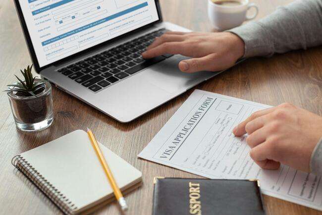 A person filling out a visa application form on a laptop while referencing a physical form, showcasing the dual nature of immigration case management.