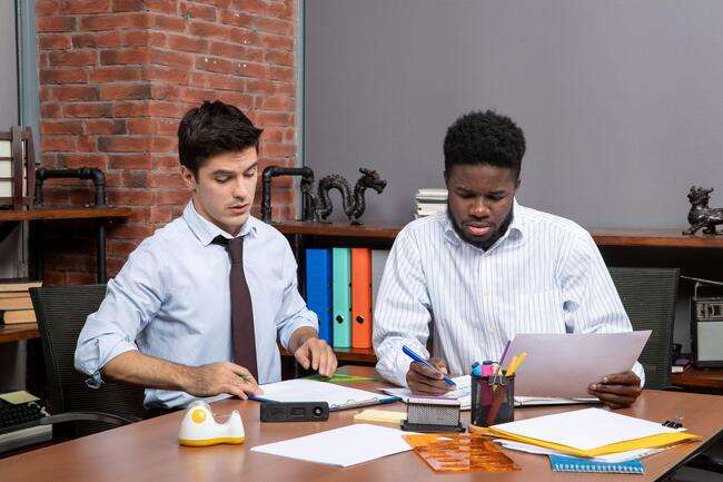 Two men working at a desk, analyzing documents in a business environment